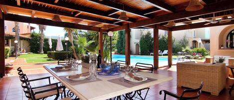 Un área de comedor al aire libre con vista a la piscina, vigas de techo de madera y mobiliario de mimbre.