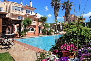 A swimming pool area with a patio, outdoor furniture, and a large building in the background. - Oasis Pool House by GHH (Saronikos)