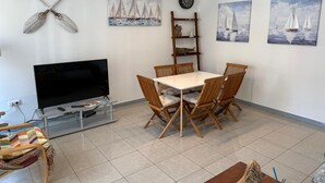 A living room with a TV, wooden dining table, chairs, and sailboat paintings on the walls.