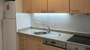 A kitchen with wooden cabinets, a white refrigerator, a stainless steel sink, a dishwasher, and an oven.