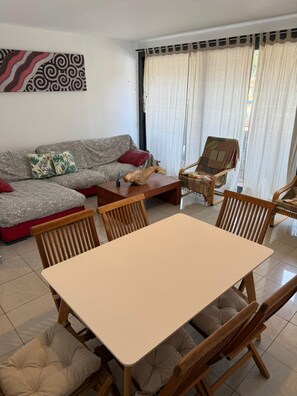 Una sala de estar con sofá, una mesa de centro, una mesa de comedor con sillas y una ventana con cortinas.