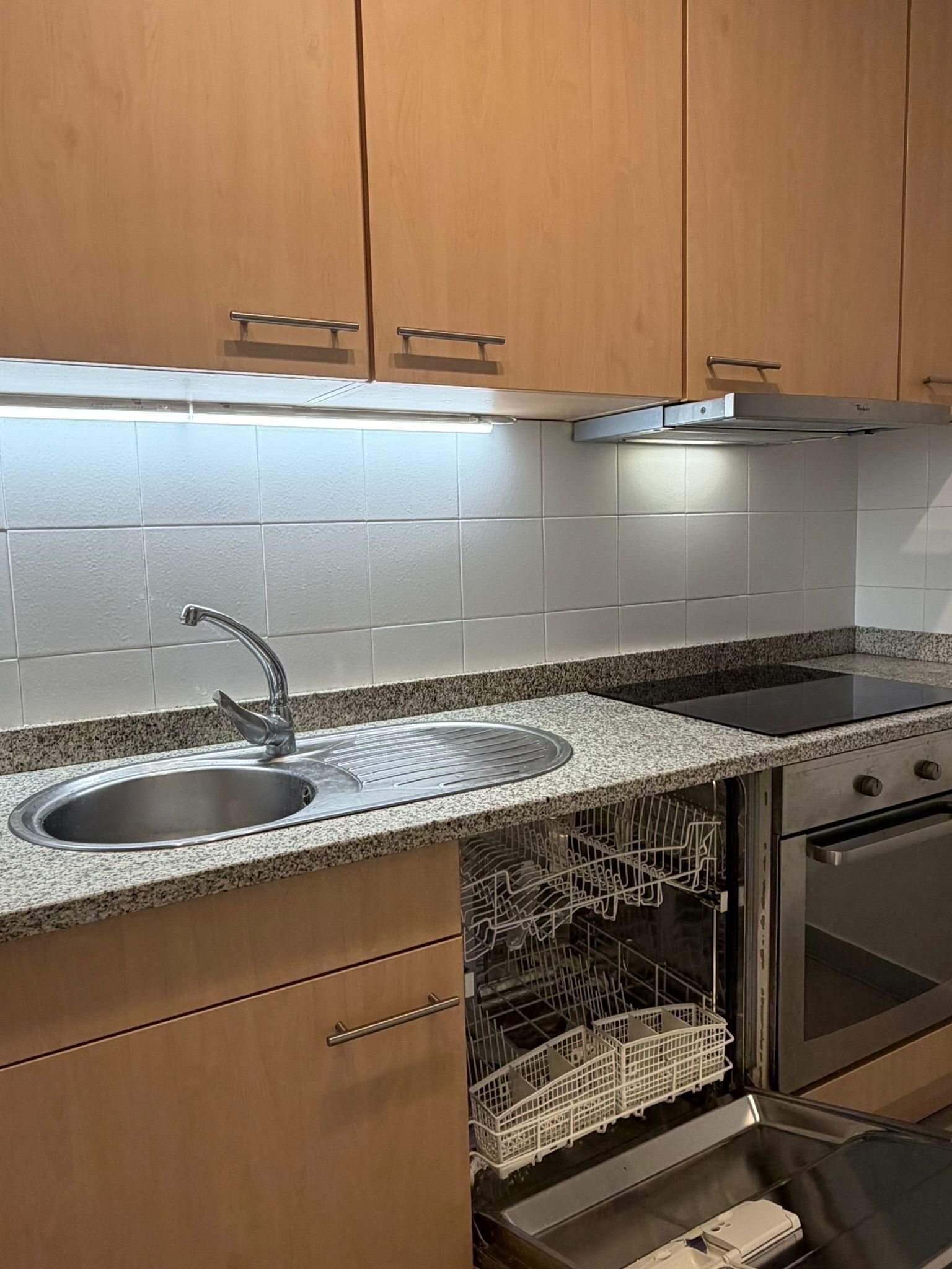 Una cocina con un lavamanos de acero inoxidable, estufa empotrada y lavavajillas.