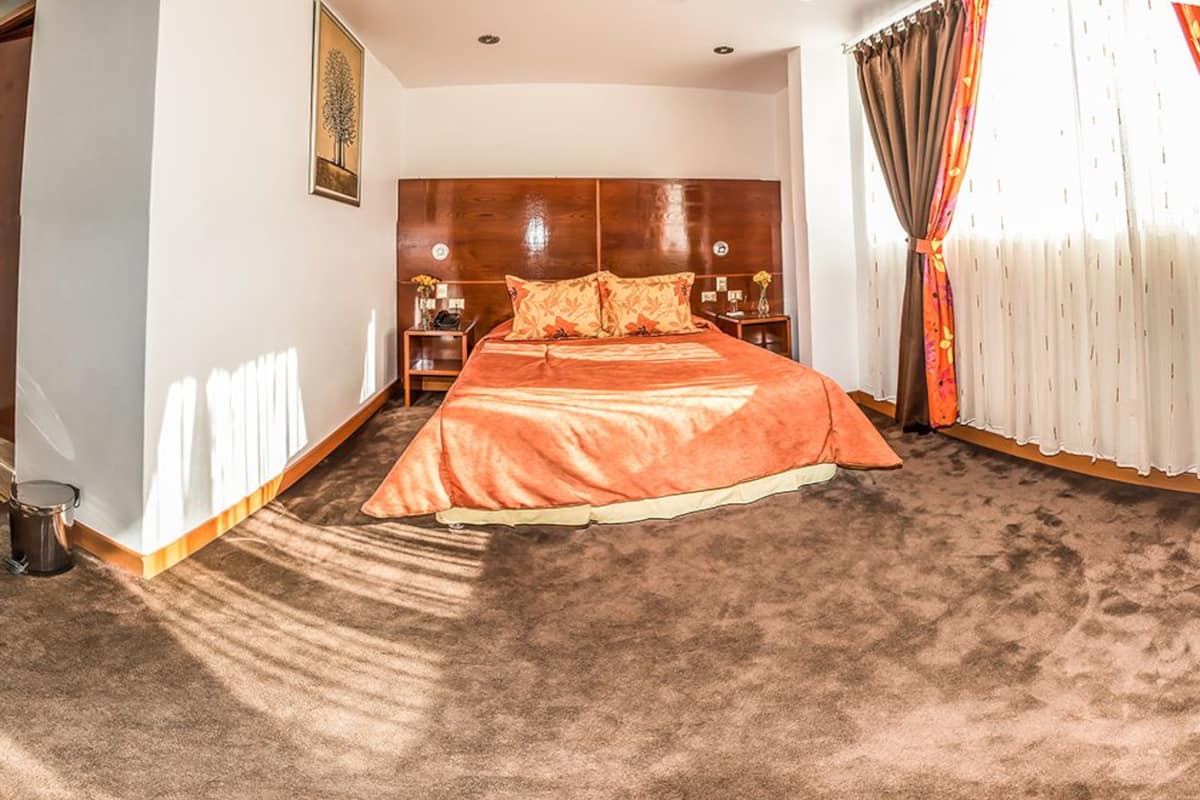 A hotel room with a large bed, a wooden headboard, a nightstand, and a window with curtains.