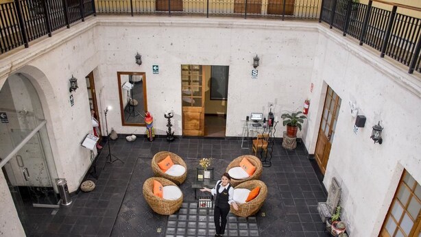 A courtyard with wicker furniture, a staff member, and a door leading to an interior space. - Hotel Tikary (Arequipa)