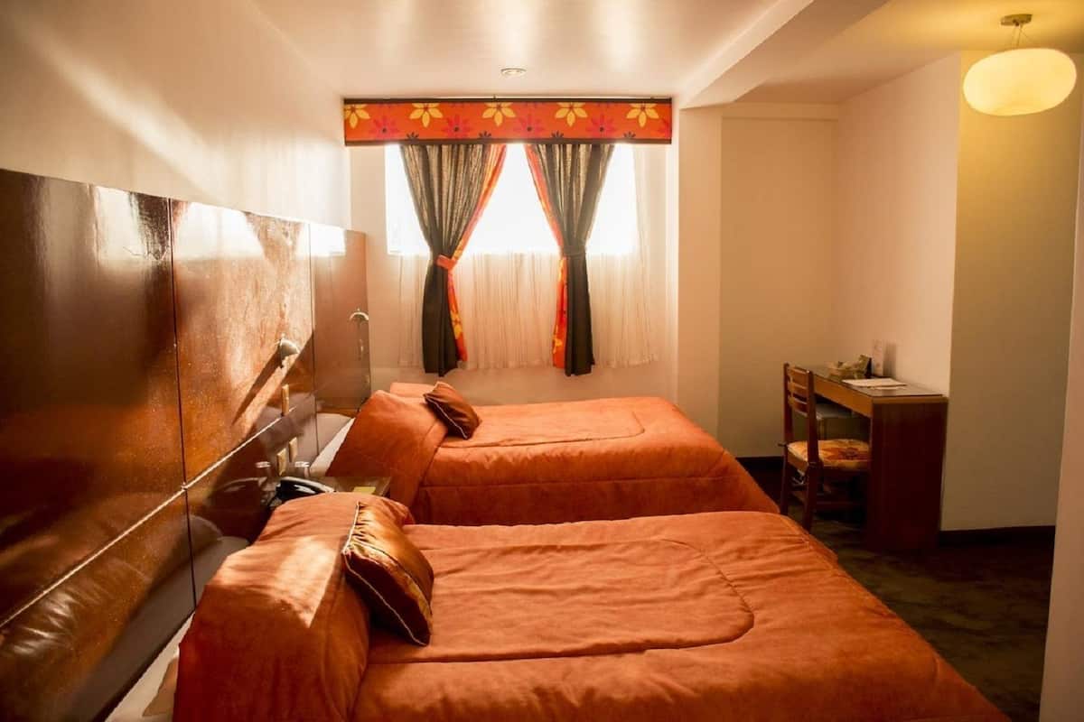 A hotel room with two beds, a desk, and a chair.