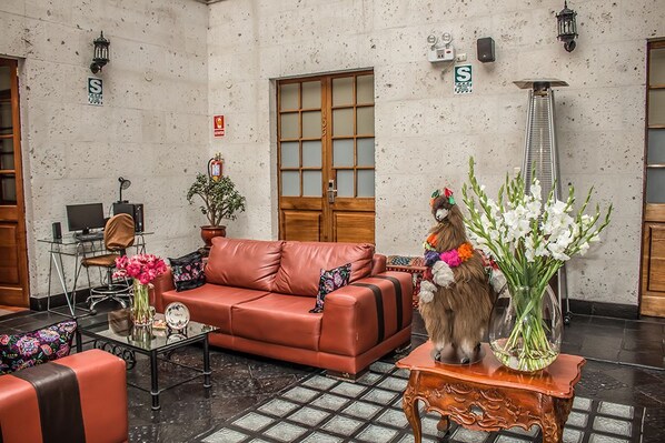 A lobby with a red leather sofa, a glass coffee table, a wooden side table with a vase of flowers, and a large window with a view of the street.