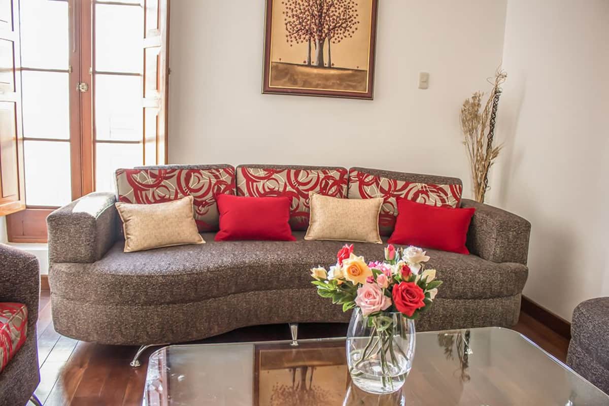 A living room with a grey sofa, red and beige cushions, a glass coffee table, and a vase with flowers.