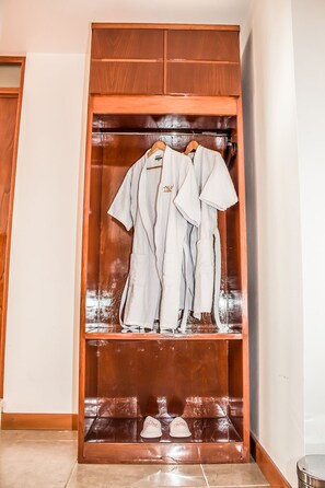 A wooden wardrobe with a mirror, containing hanging clothes and a pair of shoes.