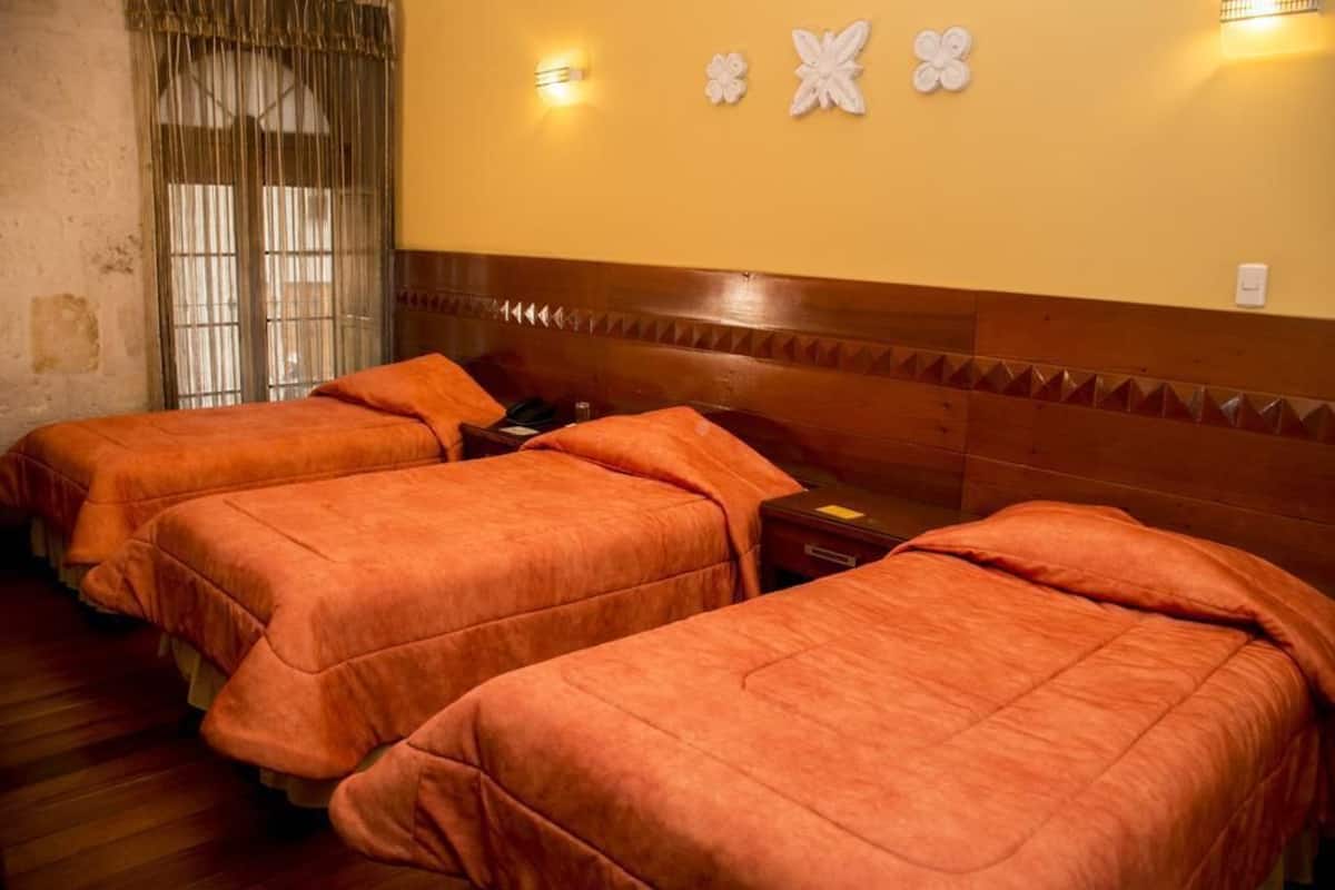 A hotel room with three beds, wooden headboard, and a window with curtains.