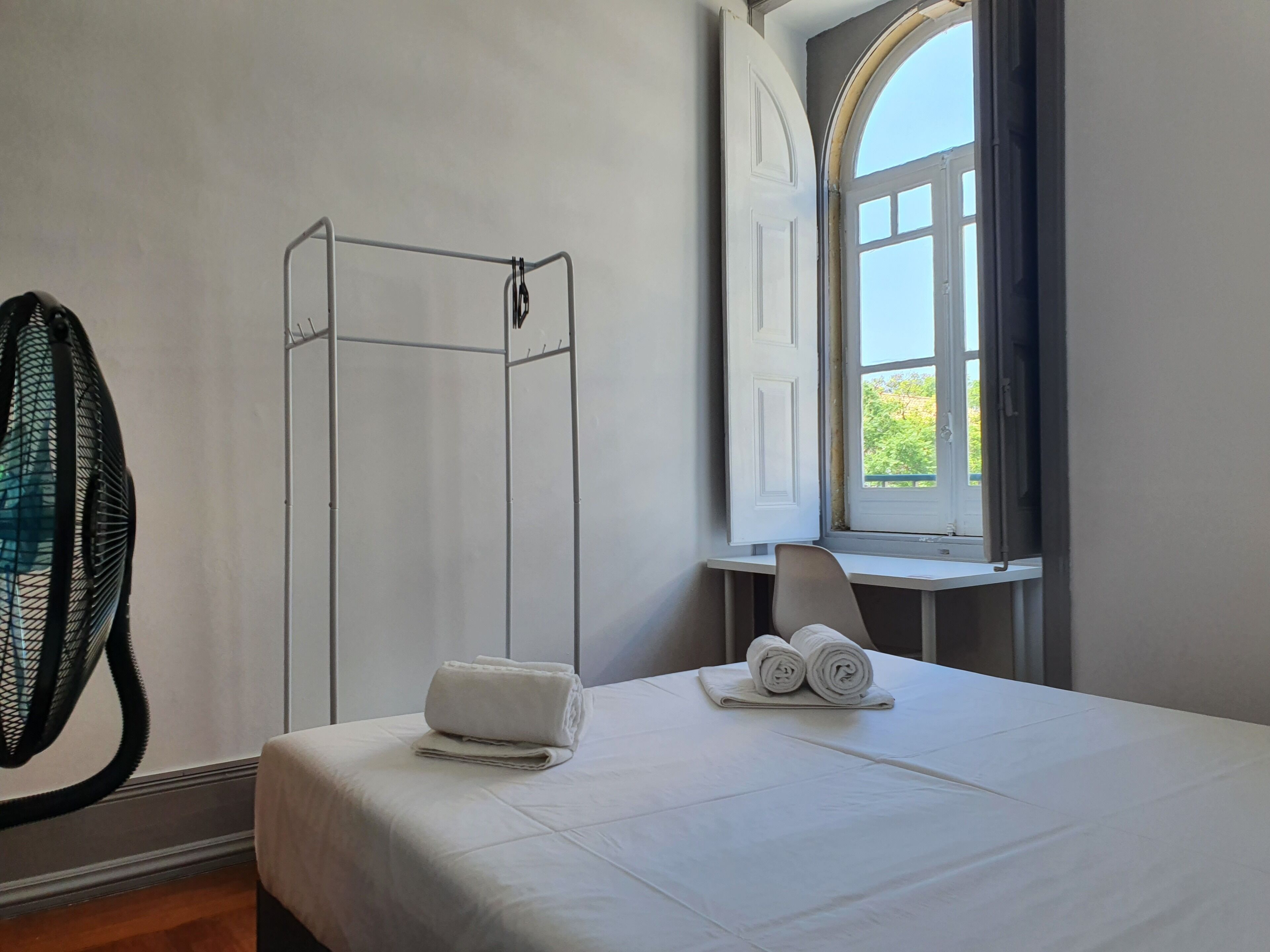 A hotel room with a bed, a window, a chair, and a towel rack.