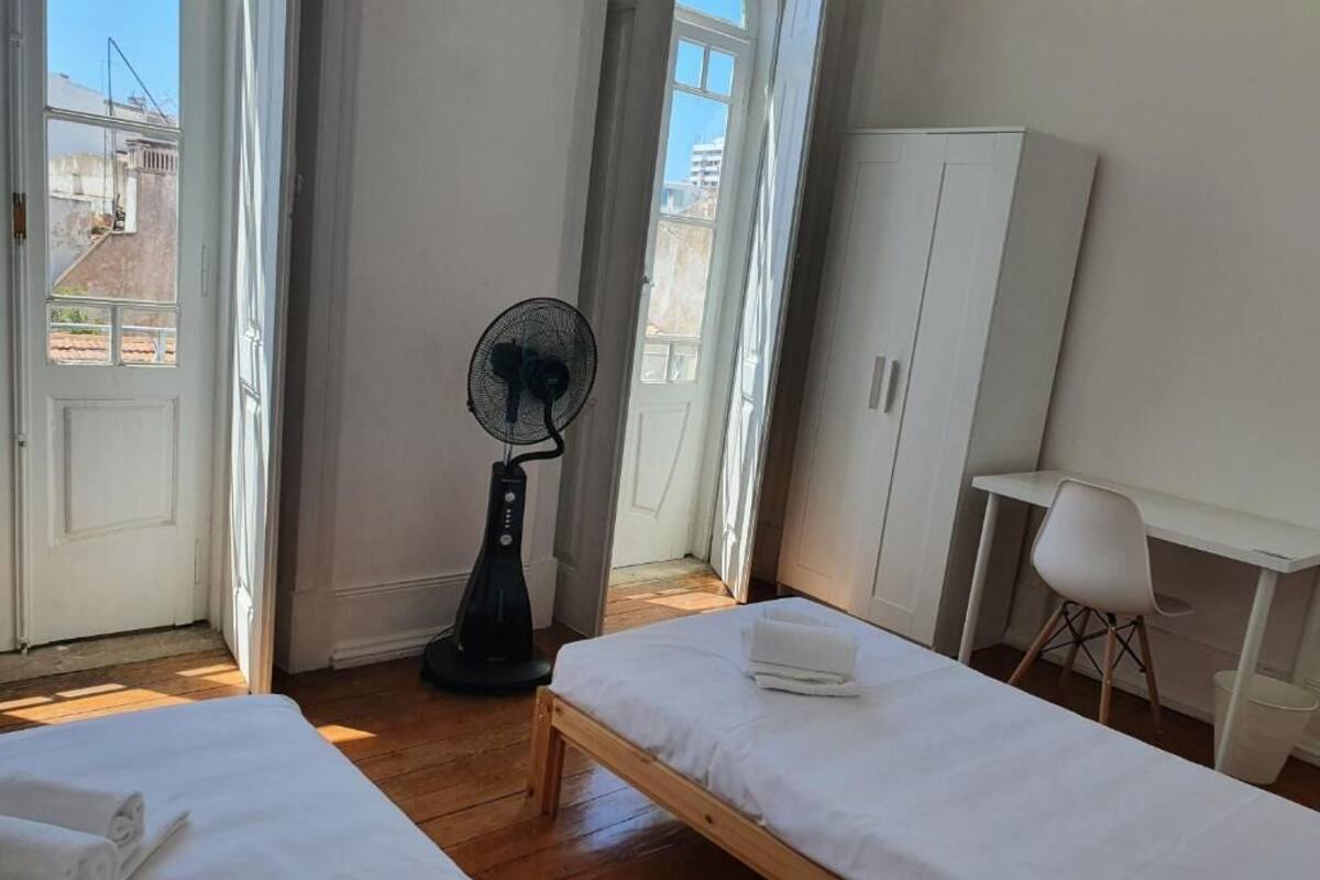 A room with two beds, a fan, a desk, and a chair.