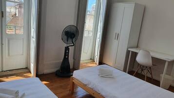 Una habitación con dos camas, un ventilador, un escritorio y una silla.