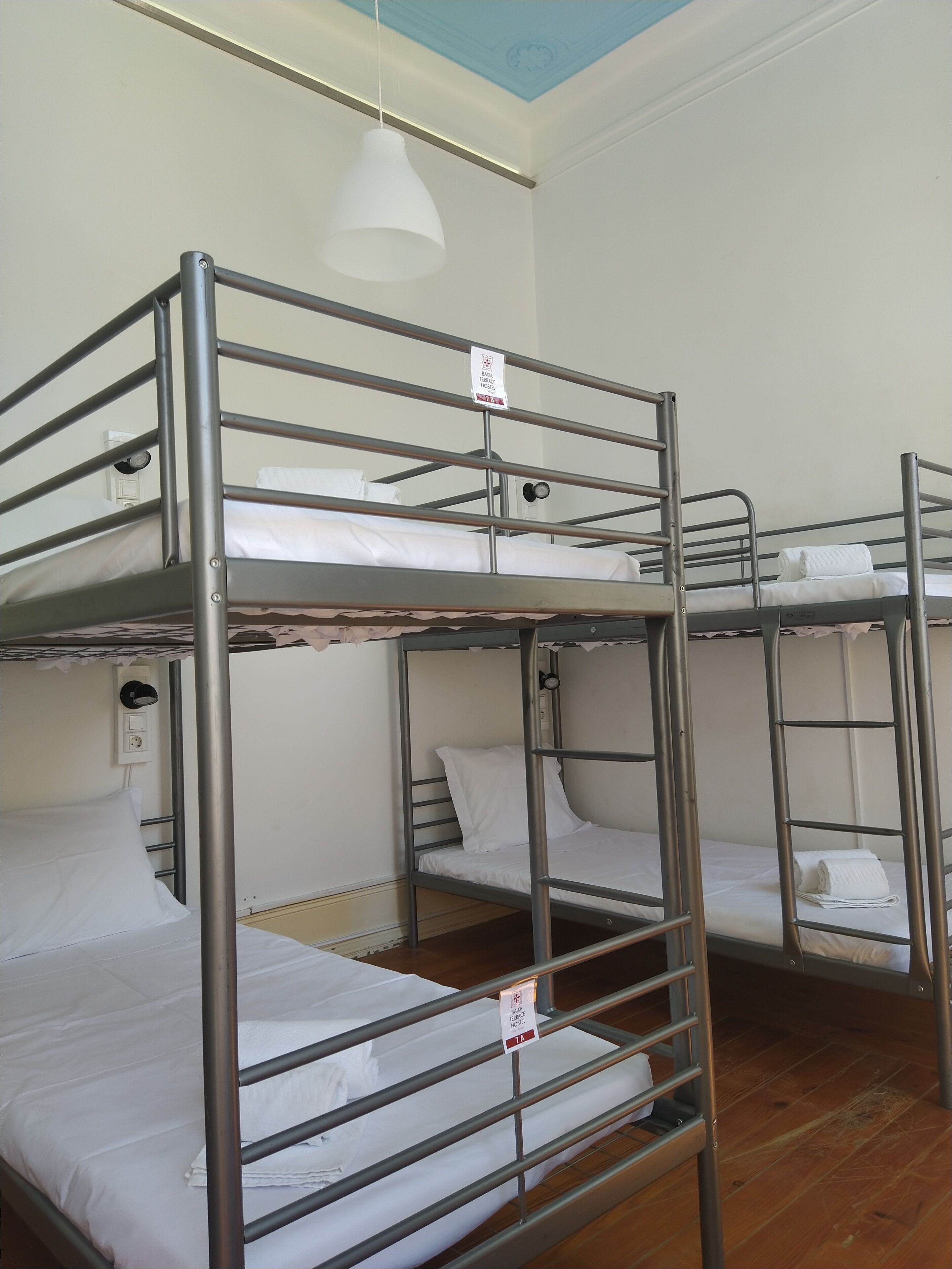 A bunk bed room with metal railings, white bedding, and a ceiling light fixture.