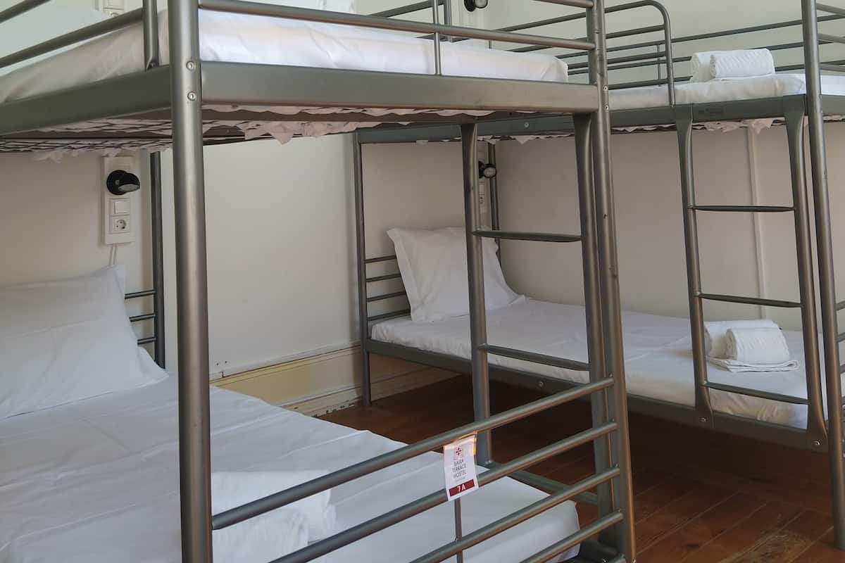 A bunk bed room with metal railings, white bedding, and a ceiling light fixture.