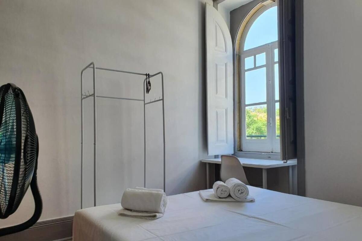 A hotel room with a bed, a window with curtains, a chair, and a towel rack.