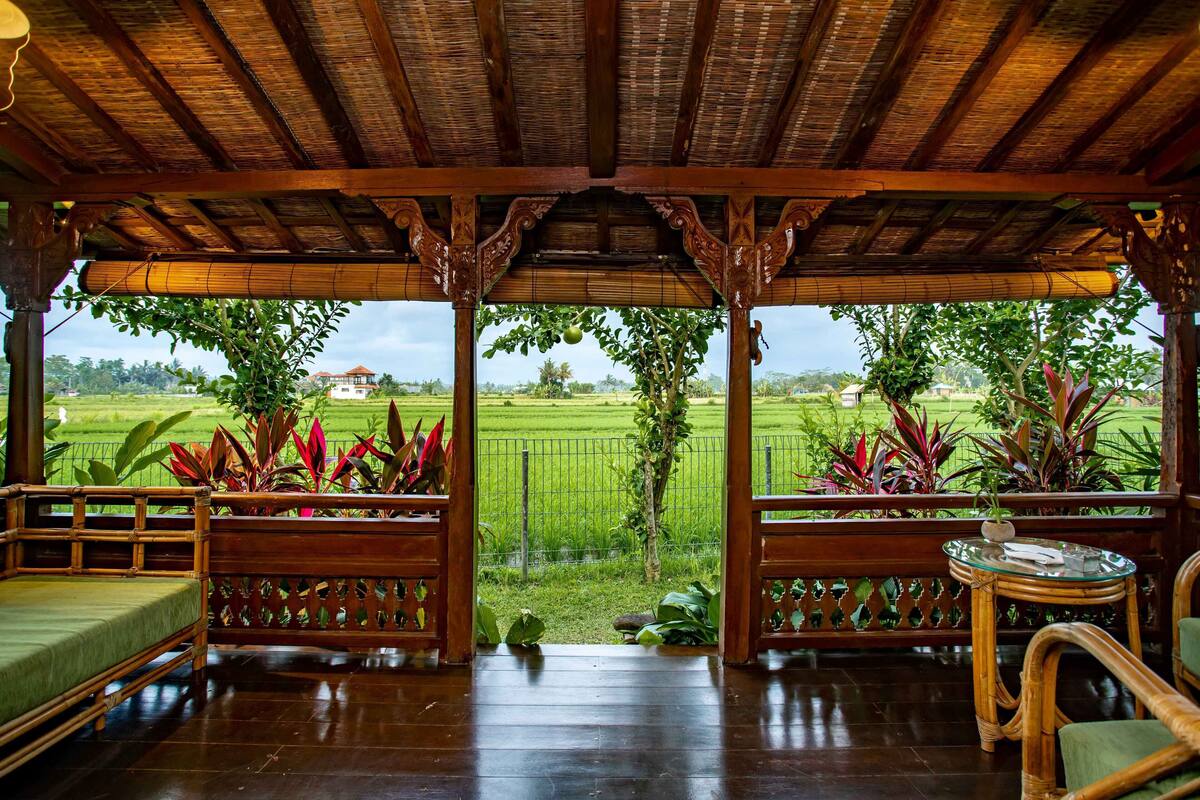 A wooden pavilion with a thatched roof, a wooden bench, and a glass table.
