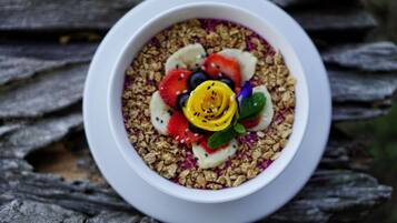 A bowl of granola with fruits and a flower on a wooden surface.