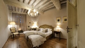 A bedroom with a large bed, two bedside tables with lamps, a chair, and a chandelier. - La Corte Di Ambra (Cortona)