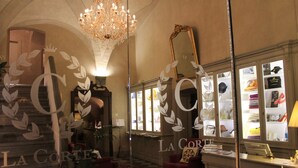 A hotel lobby with a chandelier, a mirror, and a display of items on shelves. - La Corte Di Ambra (Cortona)