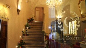 A grand staircase with potted plants, a chandelier, and a mirror reflecting the room. - La Corte Di Ambra (Cortona)