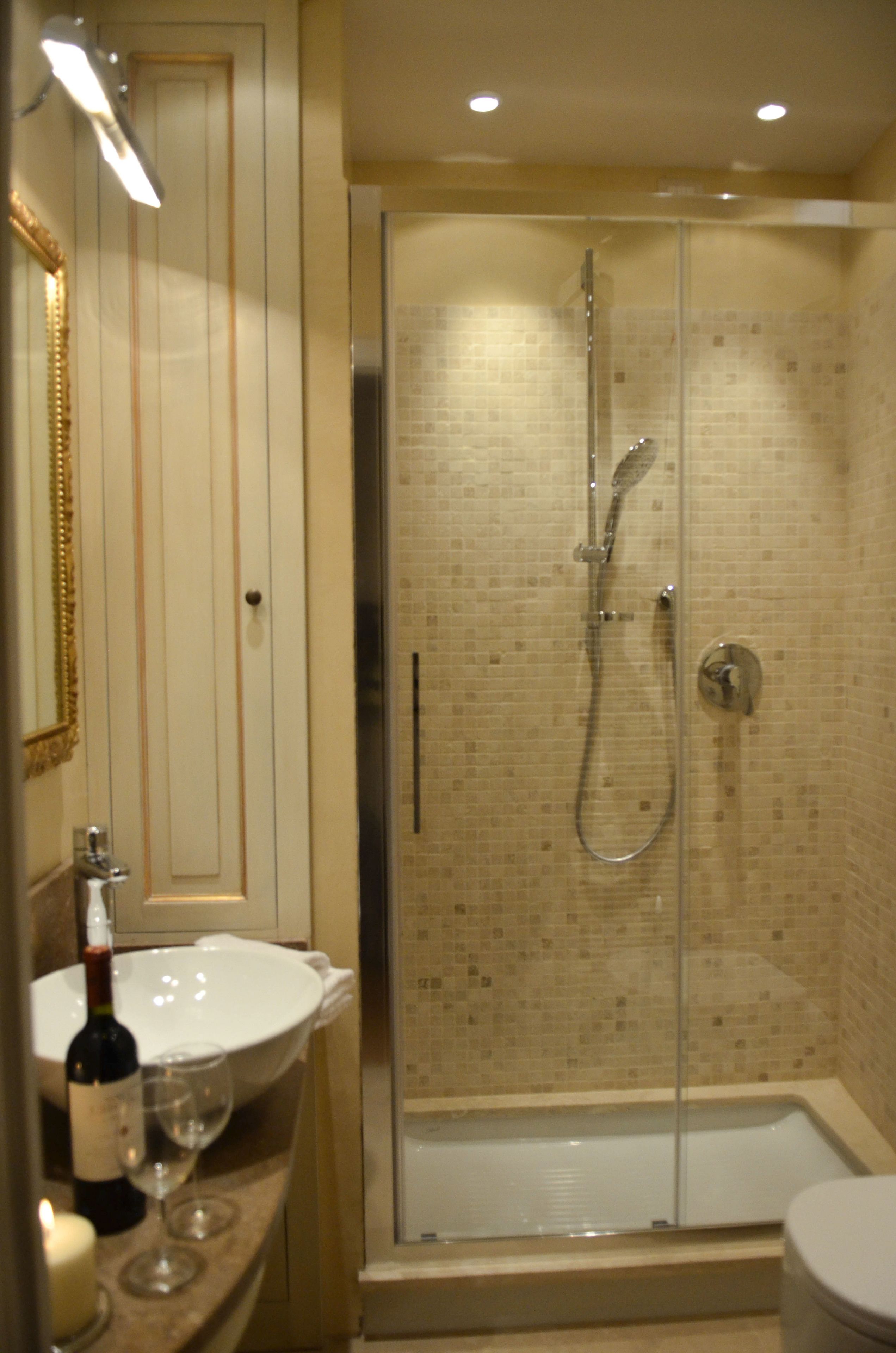 A bathroom with a glass-enclosed shower, a sink with a wine bottle and glass, and a mirror.