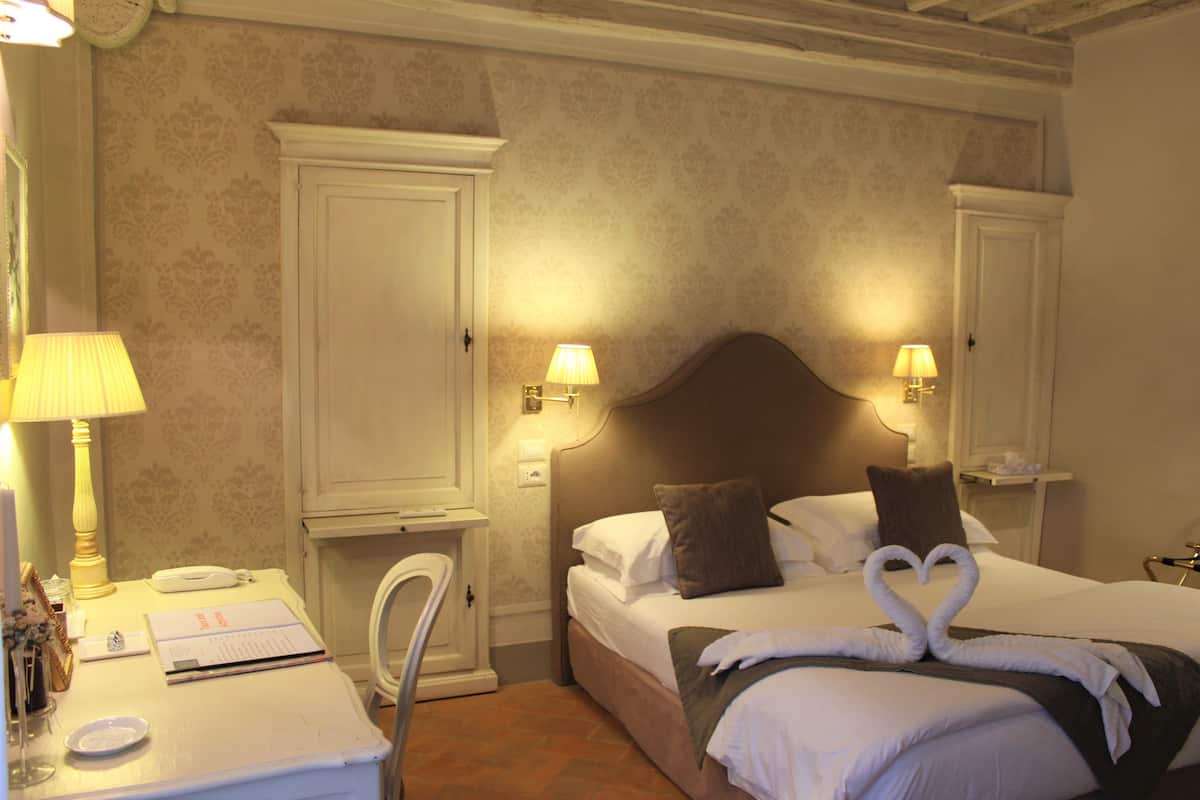 A hotel room with a bed, bedside lamps, a desk with a telephone, and a chair.