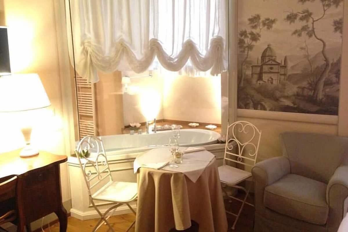 A room with a dining table, two chairs, a sofa, a window with curtains, and a painting on the wall.