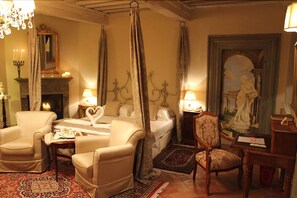 A room with a fireplace, a bed with a heart-shaped pillow, two armchairs, a wooden side table, and a painting on the wall. - La Corte Di Ambra (Cortona)