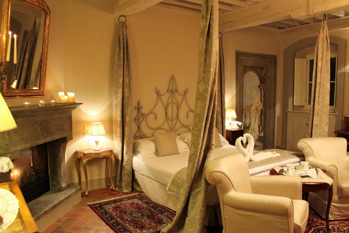 A bedroom with a four-poster bed, a fireplace, a sitting area with a table and chairs, and a large mirror.