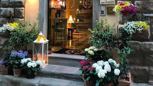 A stone archway entrance with a glass door, potted plants, and wall-mounted lights. - La Corte Di Ambra (Cortona)