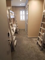 Un pasillo estrecho con literas a ambos lados, una puerta al final y una ventana con persianas.