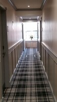 Un pasillo de hotel con alfombra a cuadros, puertas dobles y un ventanal al final.