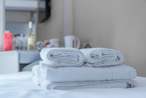 A neatly folded stack of white towels on a bed in a hotel room.