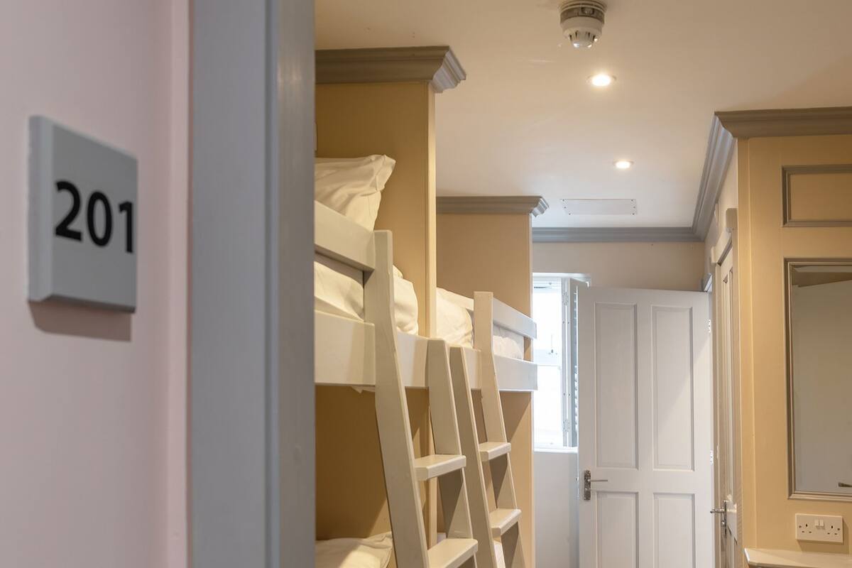 A hotel room with bunk beds, a bathroom with a mirror, and a door labeled '201'.