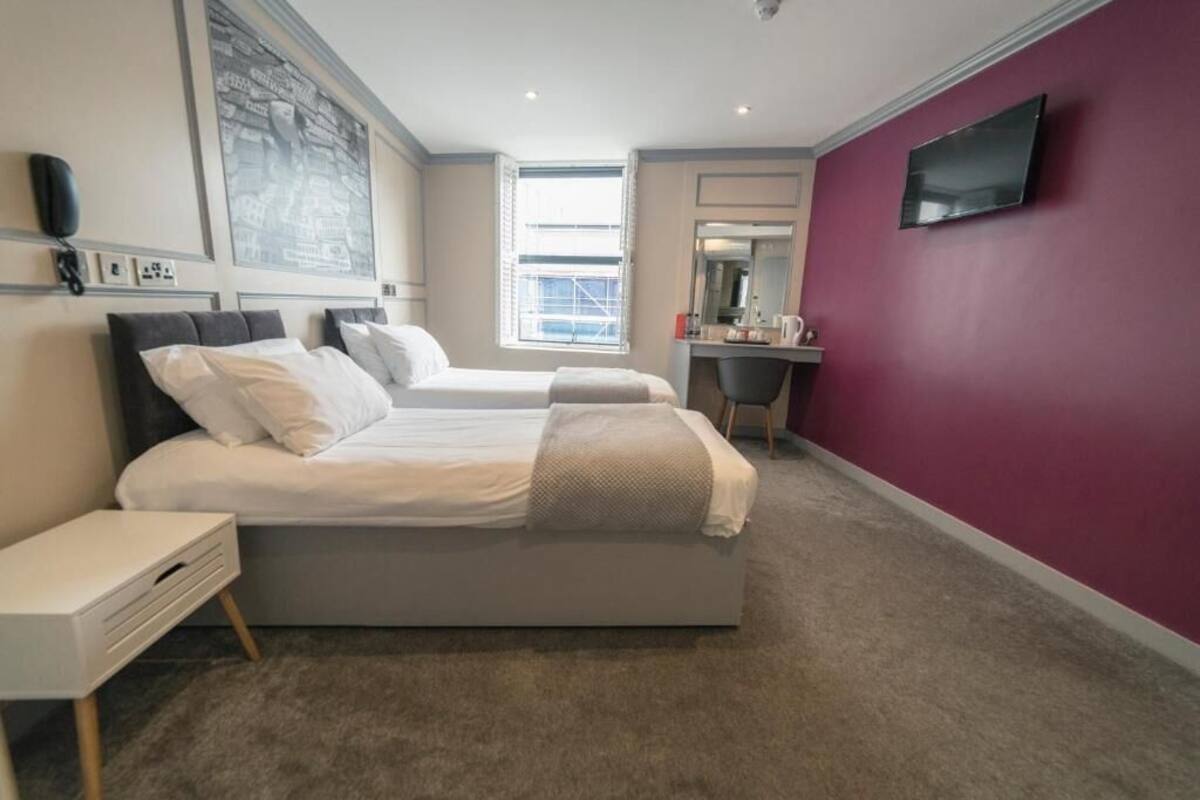 A hotel room with two beds, a desk, a TV, and a large window.