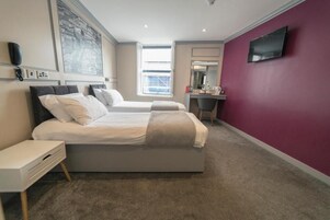 Habitación de hotel con dos camas, un escritorio, un televisor y un ventanal grande.