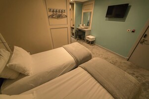 Habitación de hotel con dos camas, un escritorio con silla, un espejo y un televisor montado en la pared.