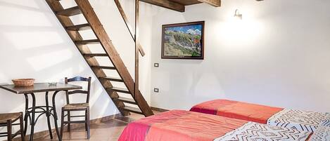 Un dormitorio con escaleras de madera, una cama con ropa de cama estampada, una mesita con una cesta y un cuadro en la pared.