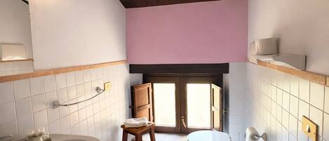 Un baño con bañera, inodoro y lavamanos, techo de madera, piso de baldosas y pared rosa.