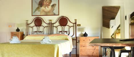 Un dormitorio con techo de madera, una cama con colcha amarilla, un aparador de madera y una mesa con sillas.