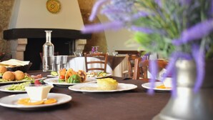 Une table à manger avec des assiettes remplies de nourriture, un vase avec des fleurs violettes et une cheminée en arrière-plan.