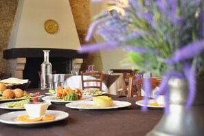 A dining table with plates of food, a vase with purple flowers, and a fireplace in the background. - Azienda Agrituristica Le Puzelle (Santa Severina)