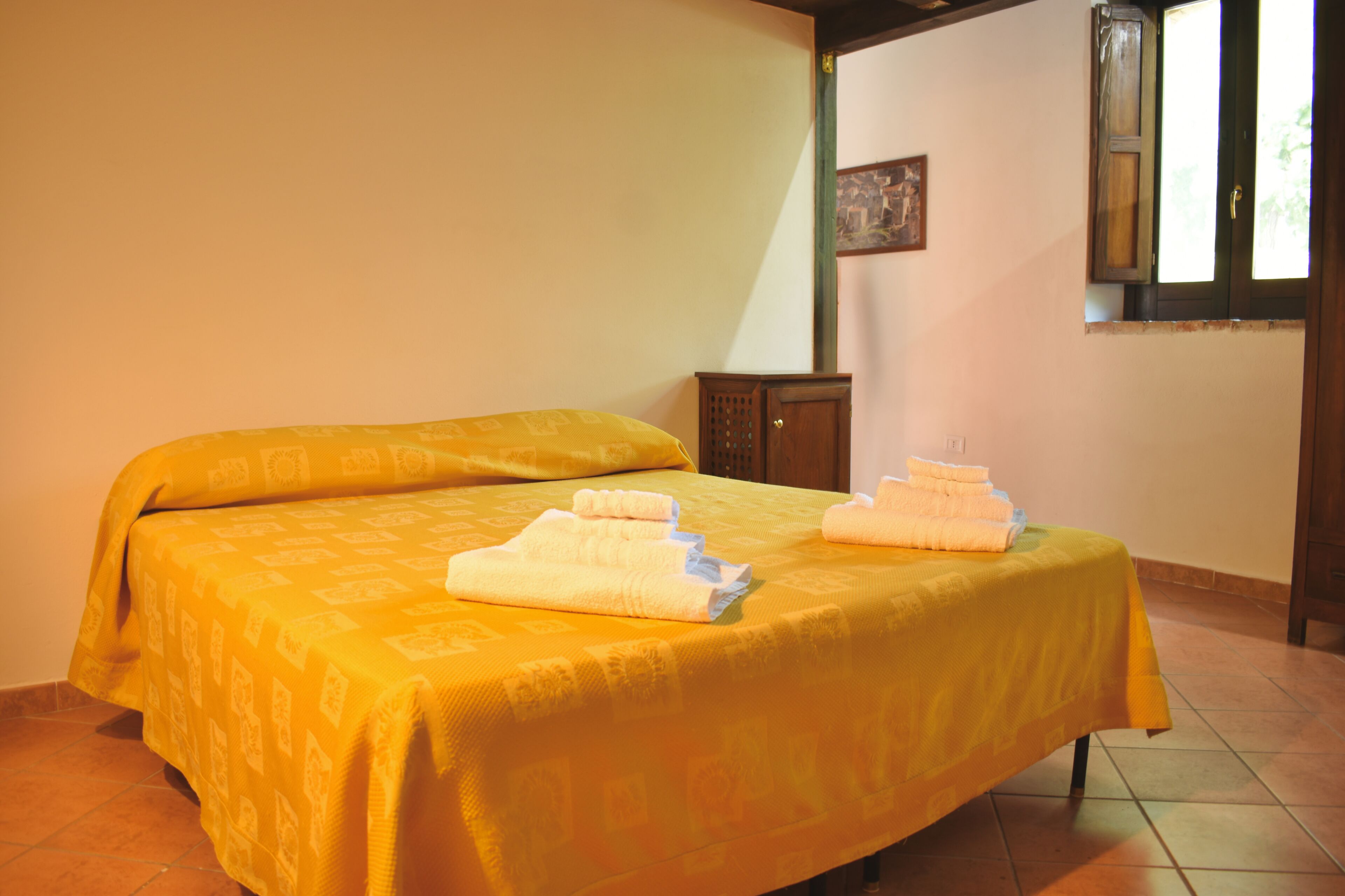 Un lit simple avec une couvre-lit jaune et deux serviettes pliées posées dessus.