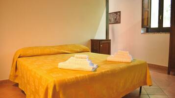 Uma cama de solteiro com um cobre-leito amarelo e duas toalhas dobradas.
