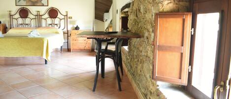 A bedroom with a bed, a wooden table, a chair, a stone wall, and a door.