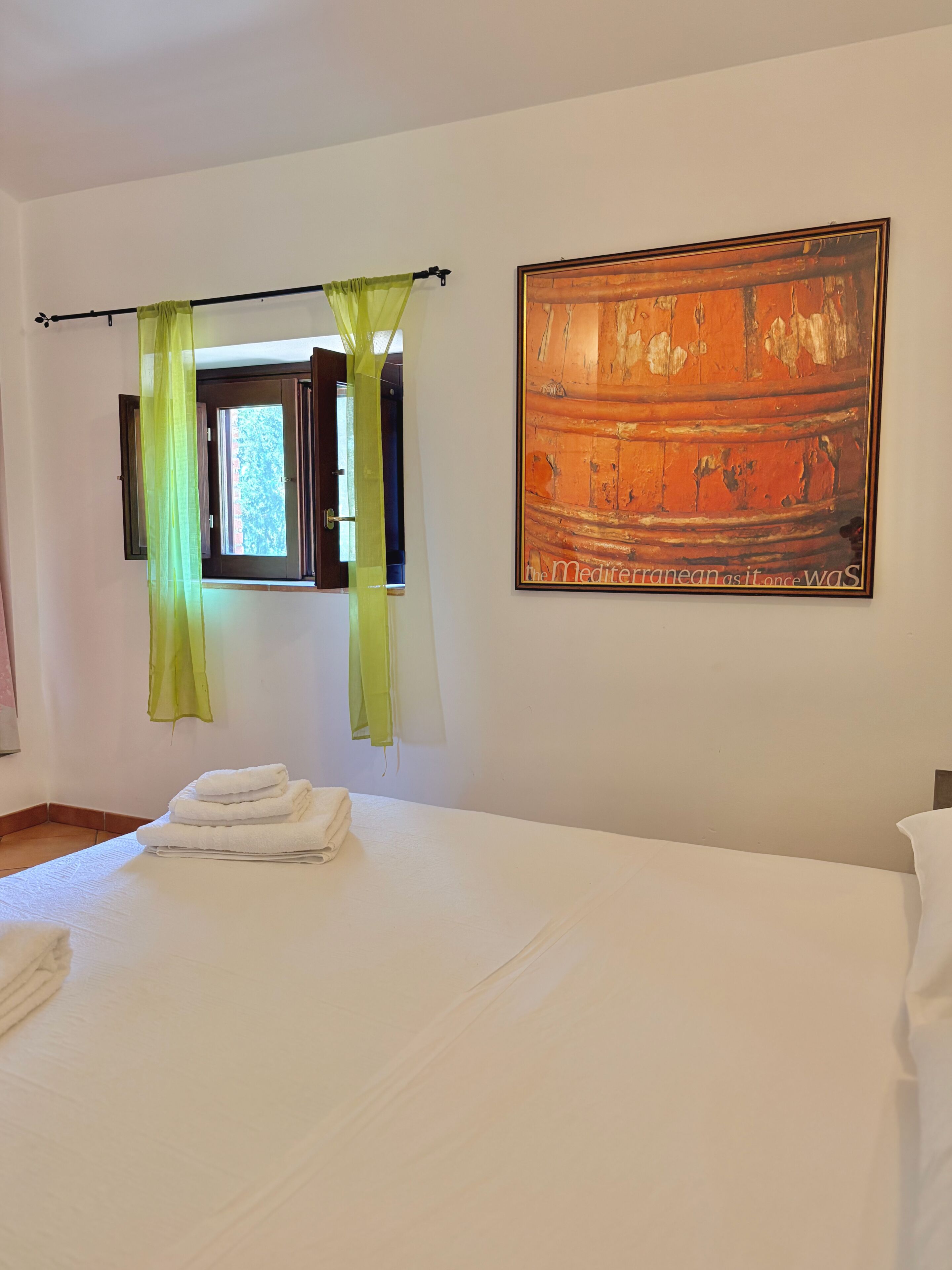 A hotel room with a bed, a window with curtains, and a painting on the wall.