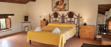 A bedroom with a bed, bedside tables, a nightstand, a painting, a window, and a wooden ceiling.