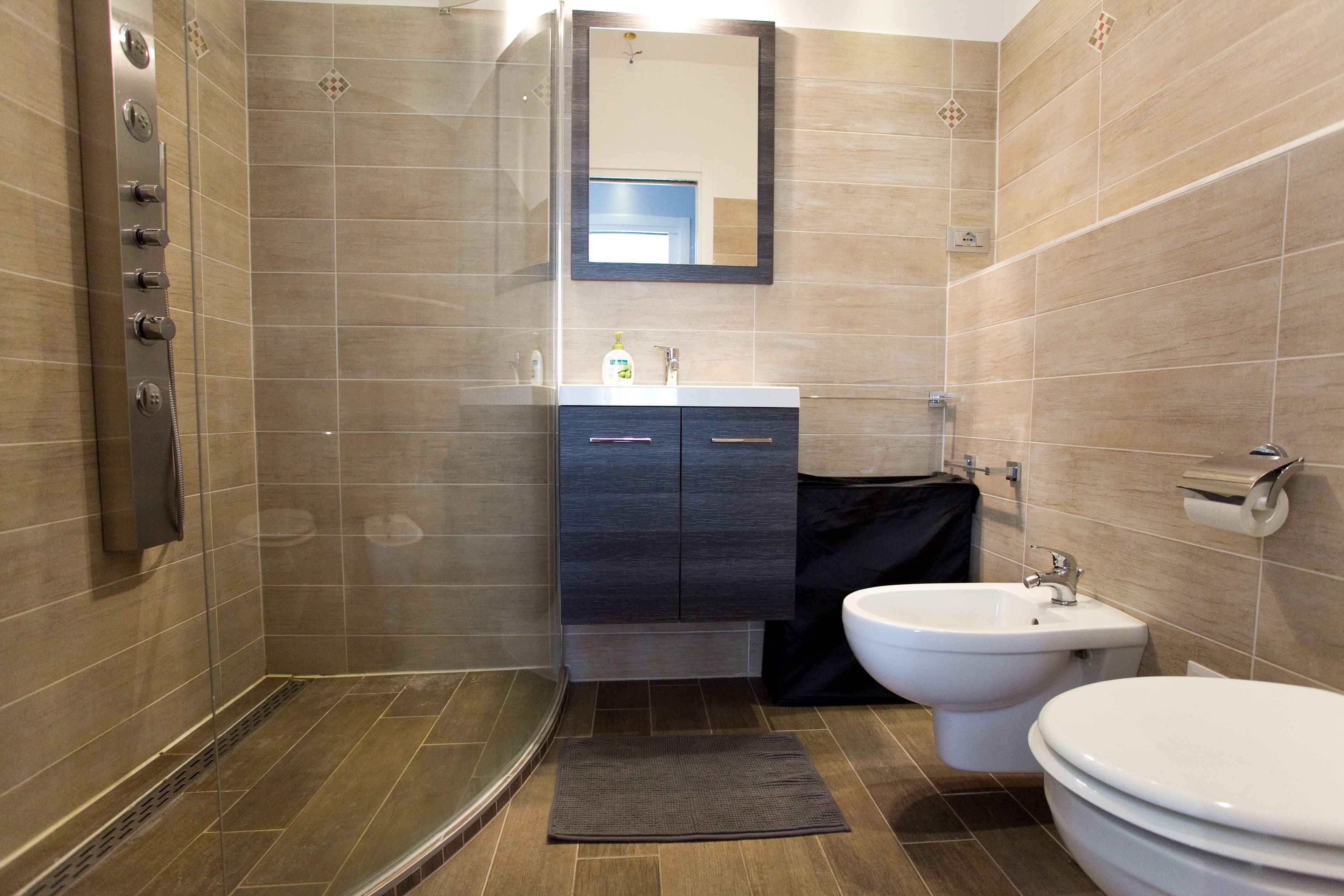 A modern bathroom with a glass-enclosed shower, a vanity with a mirror, a bidet, and a toilet.