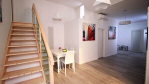 A spacious room with a wooden staircase, a dining area with a table and chairs, and a large painting on the wall. - Budapest Easy Flat - Teresa Lux Apartment (Budapest)