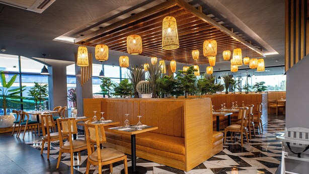Um restaurante moderno com mobiliário de madeira, uma área de estar central e luminárias de vime pendentes.